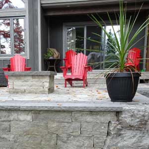Interlocking patio with red Muskoka chairs. Armour wall in front and natural stone fire pit can be seen on the left